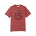 A dusty red short-sleeve t-shirt with a black graphic text print on the front that reads 'I WORK Hard SO MY CATS can live well.' with a paw print accent, displayed on a clean white background.