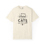 An off-white crewneck t-shirt with a black graphic text print that reads 'I WORK Hard SO MY CATS can live well.' with a paw print accent, displayed on a clean white background.