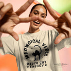Person wearing a t-shirt with 'MEOWGICAL VIBES BLACK CAT ENERGY' text and design, making a peace sign.