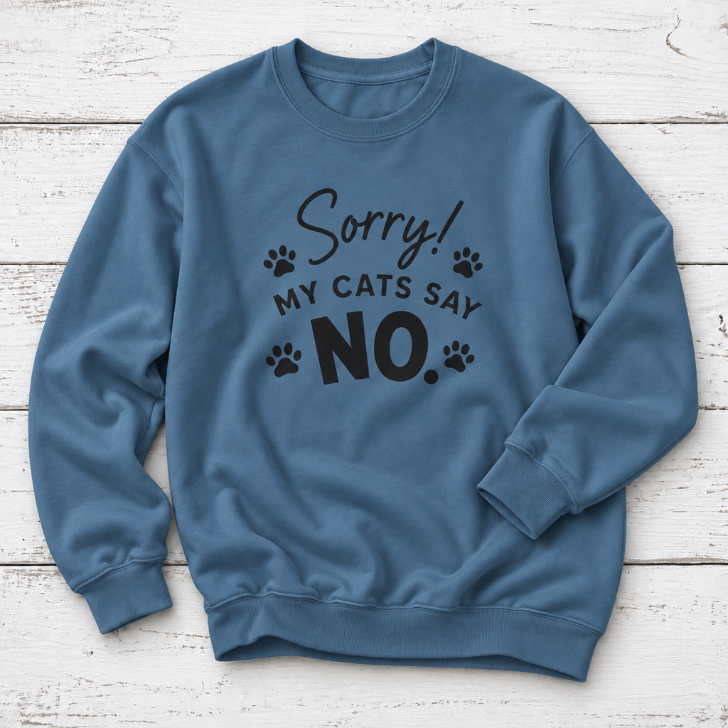A slate blue crewneck sweatshirt with a black graphic print that reads 'Sorry! MY CATS SAY NO.' accompanied by small paw prints, laid flat on a white wood plank background.