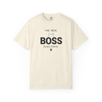 A cream-colored short-sleeve t-shirt with a graphic on the front that reads 'THE REAL BOSS lives here.' in black text, featuring a small blue and black cat outline and paw print.