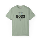 A sage green short-sleeve t-shirt with black Arabic calligraphy printed on the chest, displayed flat against a plain white background.