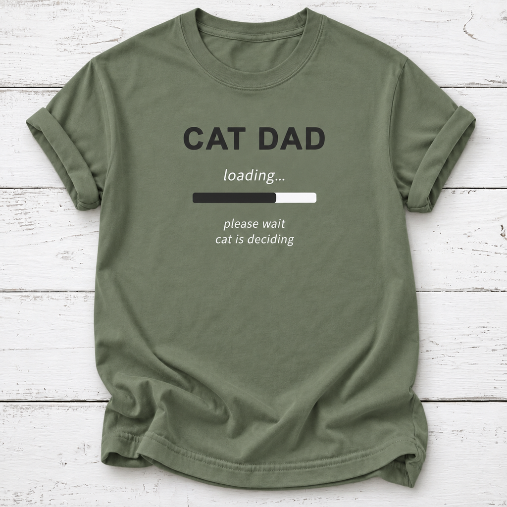 An olive green crewneck t-shirt with a 'CAT DAD' graphic print, laid flat on a white wood plank background.