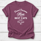 A mauve short-sleeve t-shirt with a white graphic text print reading 'Proud Pawsome Mom of the BEST CATS ever Fur real.' with a paw print, laid flat on a white wood plank background.