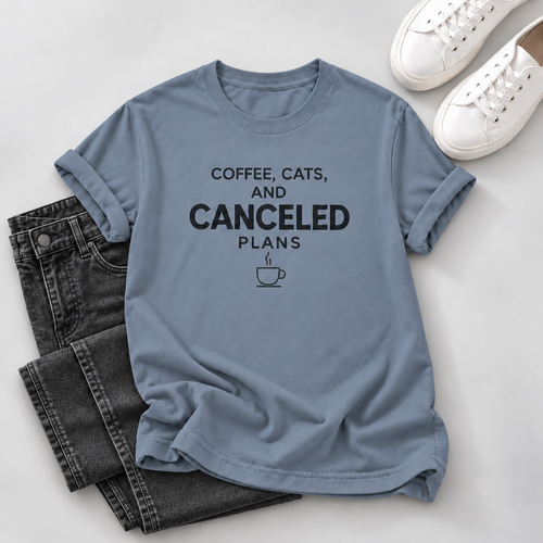 A light blue graphic t-shirt with the text 'COFFEE, CATS, AND CANCELED PLANS' and a coffee cup icon, styled in a flat lay with black jeans and white sneakers on a light gray background.