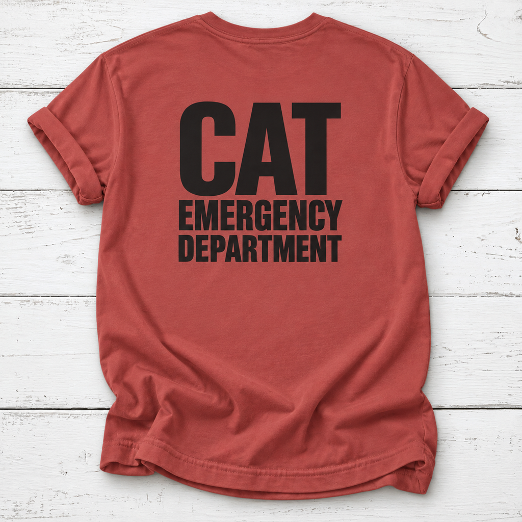 A rust-red t-shirt with 'CAT EMERGENCY DEPARTMENT' printed in bold black letters on the back, laid flat on a white wood plank background.