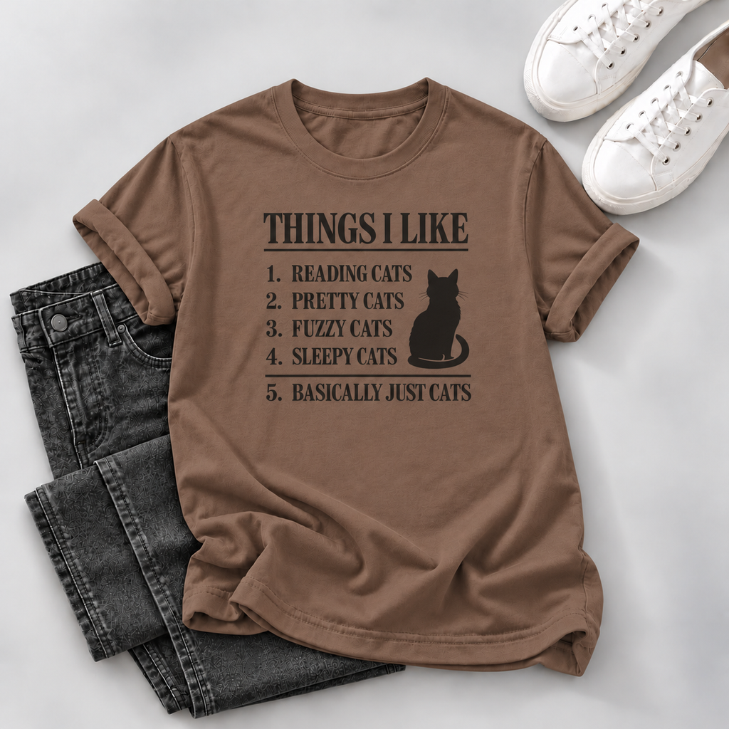 Brown T-shirt with a black cat silhouette and “Things I Like” cat-themed list, styled with dark jeans and white sneakers on a gray background.