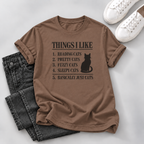 Brown T-shirt with a black cat silhouette and “Things I Like” cat-themed list, styled with dark jeans and white sneakers on a gray background.