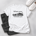 White T-shirt with “When your cat boss harasses you” lettering and a lounging black cat graphic, styled with dark jeans and white sneakers