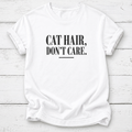 A white short-sleeve crewneck t-shirt with the text 'CAT HAIR, DON'T CARE.' printed in black serif font on the chest, laid flat on a white wood plank background.