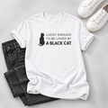 White T-shirt with a black cat silhouette and “Lucky Enough to Be Loved by a Black Cat” lettering, styled with dark jeans and white sneakers.