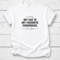 A white short-sleeve crewneck t-shirt with black printed text reading 'I certify: MY CAT IS MY FAVORITE COWORKER. Cat Lover' laid flat on a white wood plank background.