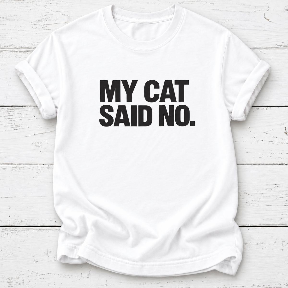White T-shirt with bold black “My Cat Said No.” lettering and rolled sleeves, laid flat on white wooden boards.
