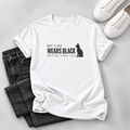 A white short-sleeve graphic T-shirt laid flat on a light gray surface, styled with folded dark gray jeans and white sneakers. The shirt has black text reading 'MY ORANGE CAT HAS A LOT TO SAY' with a soundwave graphic below.